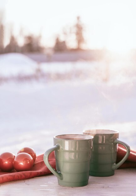 Green porcelain cups of tea on white wooden table decorated with red Christmas balls