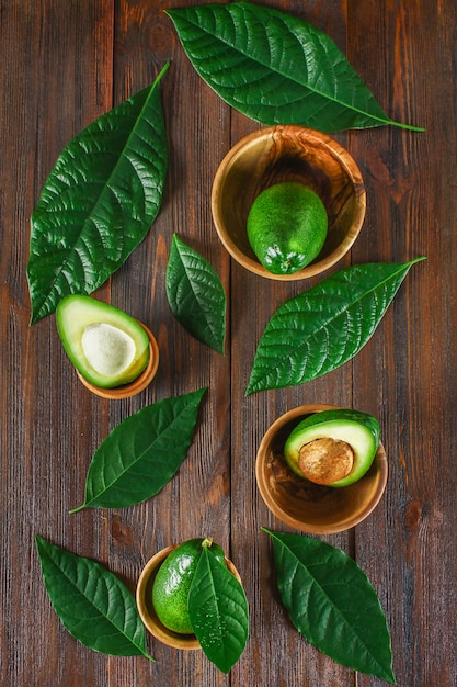 Green raw ripe cut and whole avocado fruits with stone lie in wooden bowls