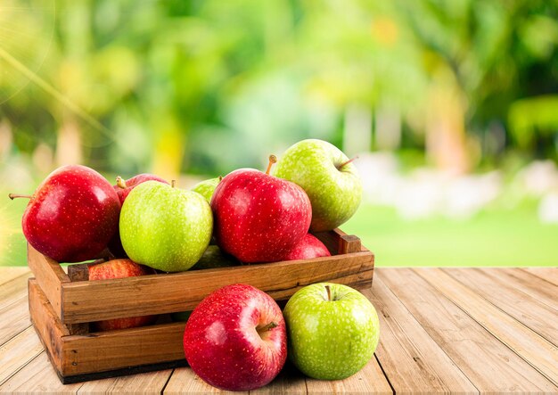 Photo green and red apples in a basket placed on wood in the park