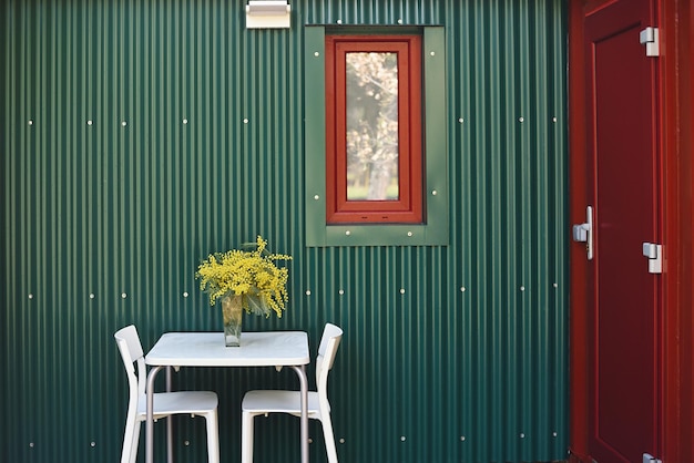 Green and red exterior of a container house with furnished entrance and flowers