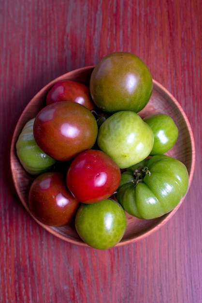Green red fresh tomatoes in wood bowl on the red table