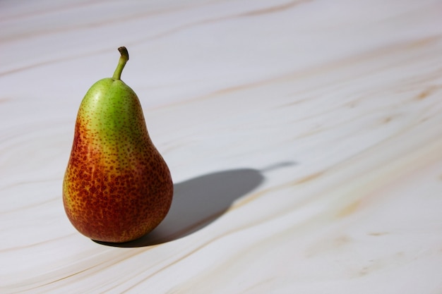 a green and red pear on a pink marble countertop casts a shadow to the right. 