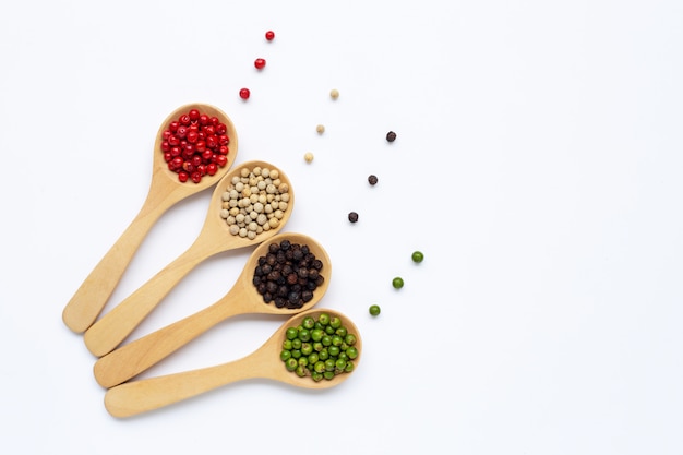 Green, red white and black peppercorns with wooden spoon on white