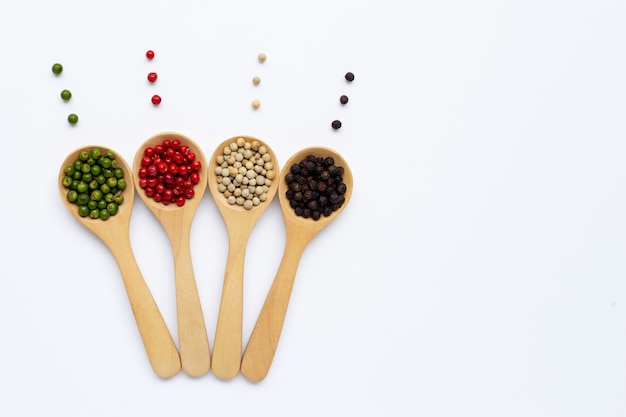 Green, red, white and black peppercorns with wooden spoon on white