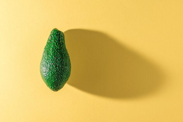 Green ripe avocado on a yellow background. delicious tropical vegetable. flat lay.