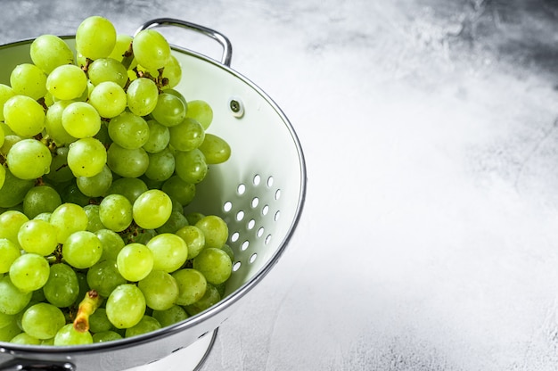 Green ripe grapes in a colander, fruits of autumn. White background.