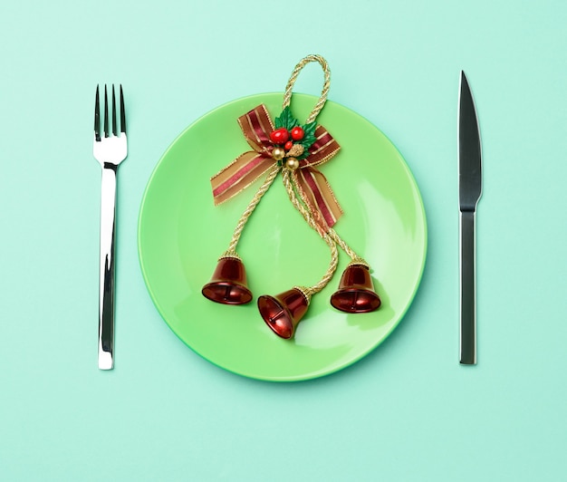 Green round red ceramic plate, knife and fork on green background, festive table setting for christmas and new year, top view