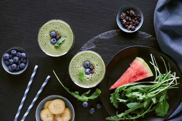 Green rucola, banana and watermelon smoothie in glass jars on dark slate ,