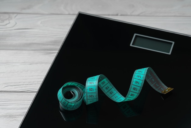 Green ruler tape on digital bathroom weight scale on wooden background