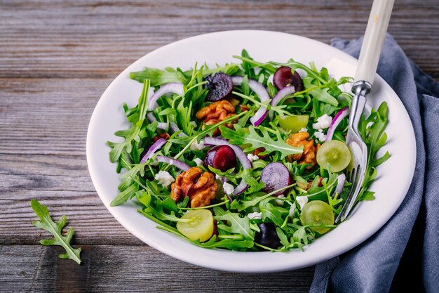 Green salad bowl with arugula walnuts goat cheese red onion and grapes on wooden background