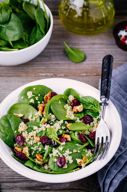 Green salad bowl with spinach quinoa walnuts and dried cranberries on wooden background