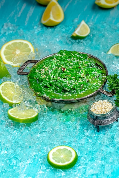 зеленый салат из чуки с посыпанными семенами кунжута, лежит в деревенской винтажной тарелке, синий морской лед