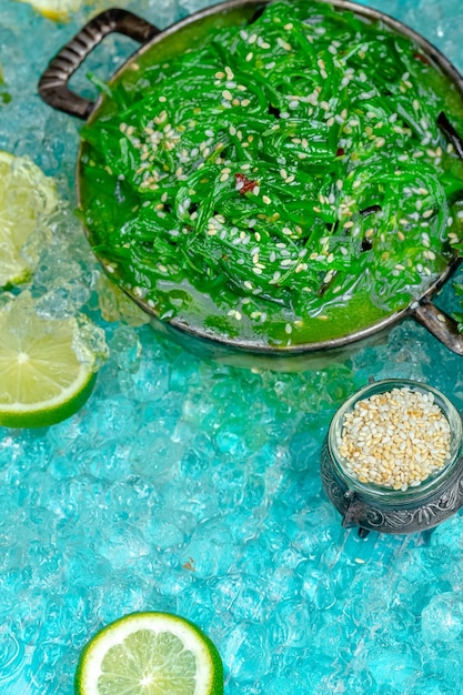 зеленый салат из чуки с посыпанными семенами кунжута, лежит в деревенской винтажной тарелке, синий морской лед