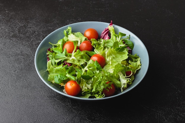 Green salad leaves with cherry tomatoes in bowl on black table