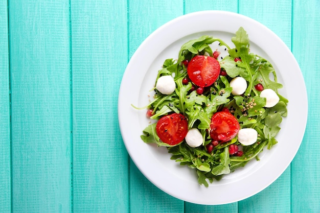 Green salad made with arugula tomatoes cheese mozzarella balls and sesame on plate on color wooden background