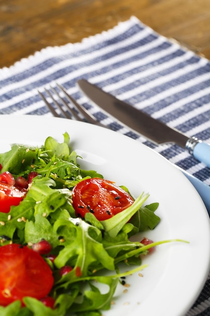 Зеленый салат из помидоров рукколы и кунжута на тарелке на деревянном фоне
