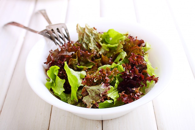 Green salad in a white bowl on a white wooden background