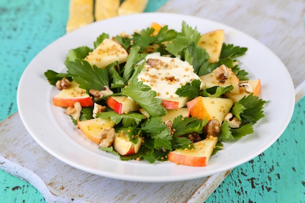 Green salad with apples walnuts and cheese on color wooden background