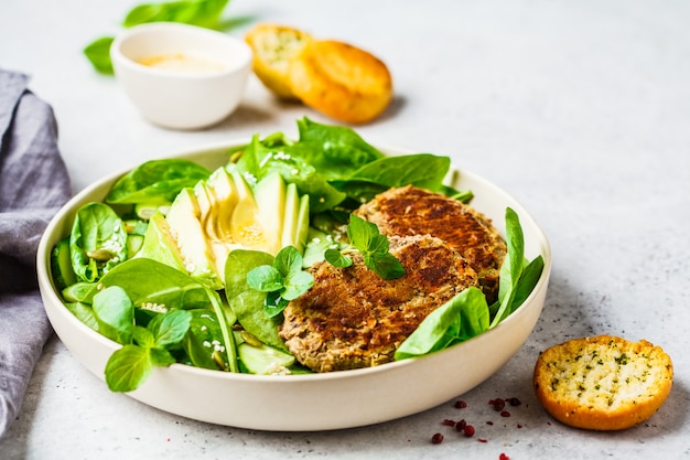 Green salad with avocado, cucumber and lentil patties in white plate.