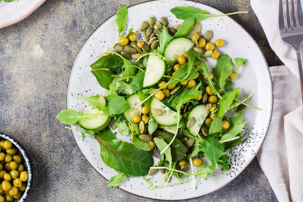 Green salad with cucumber, peas and arugula, mizuna and chard leaves on a plate on the table. Vitamin and healthy food. Vegetarian and Flexetarian Diet. Top view. Close-up