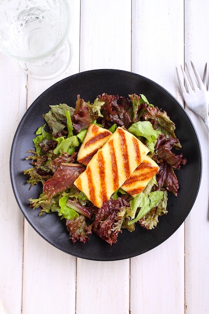 Green salad with fried halloumi cheese on a black plate