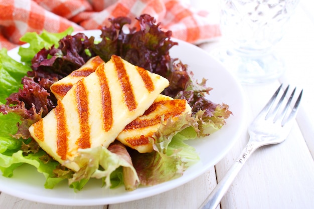 Зеленый салат с жареным сыром халуми в белой тарелке на белом фоне деревянные