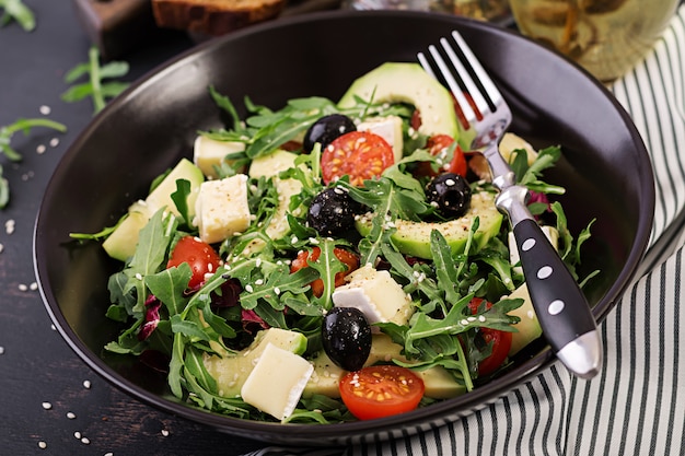 Green salad with sliced avocado, cherry tomatoes, black olives and cheese. Healthy diet vegetarian summer vegetable salad. Table setting. Food concept.