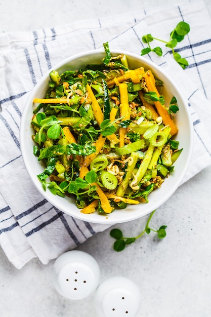 Green salad with spinach, pepper, cucumber, pesto sauce and sprouts in white bowl.