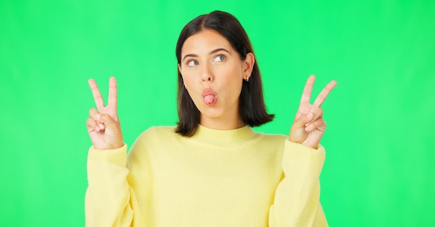 Green screen funny face expression and happy woman posing with tongue out peace sign and carefree personality Portrait female model and smile in studio with emoji reactions meme and happiness