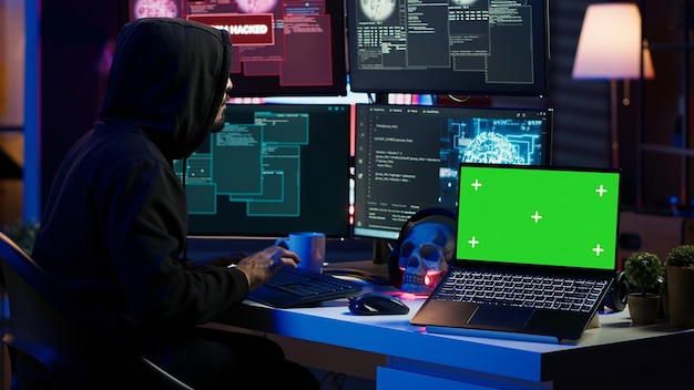 Green screen laptop used by hacker in underground hideout to write lines of code