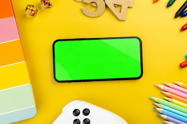 Green screen on the smartphone yellow background with school\
supplies children\'s accessories video game controller chroma\
key