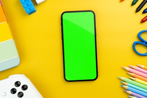 Green screen on the smartphone Yellow background with school supplies children's accessories video game controller Chroma Key