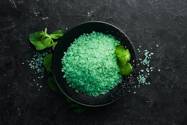 Green sea salt in a bowl On a black stone background Spa treatments Top view Free space for your text