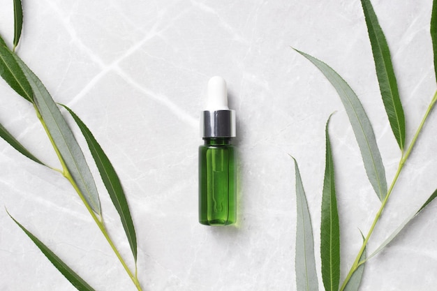 Green serum bottle with branch leaves on marble background Beauty concept for face and body care