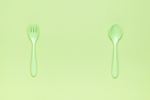 A green set of plastic forks and spoons on a green background A place for your text Flat lay