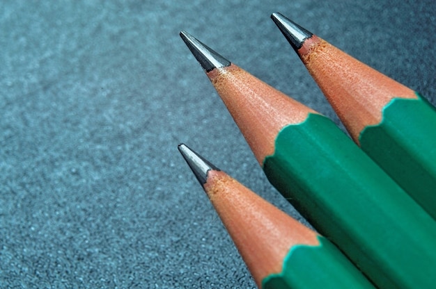 Green sharpened wooden pencils with black lead on a dark textured background. close-up.