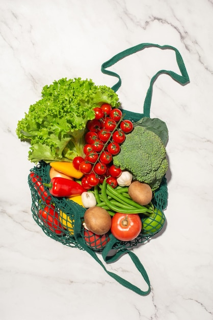 Green shopping bag with groceries on a gray marble background Eco friendly packaging