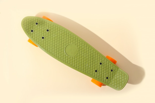 Green skateboard with orange wheels on beige. Plastic mini cruiser board. 