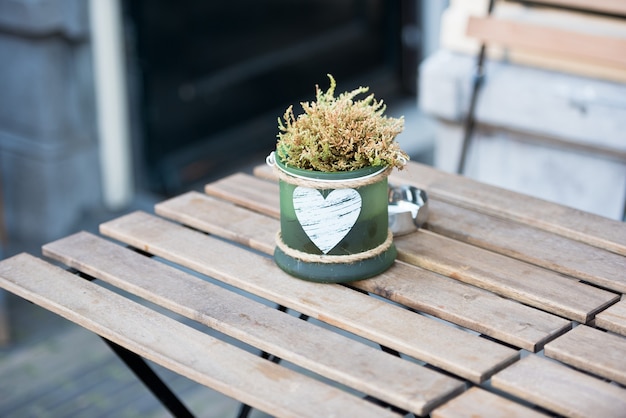 Green small pot with flowers and heart on the table in an outdoor cafe