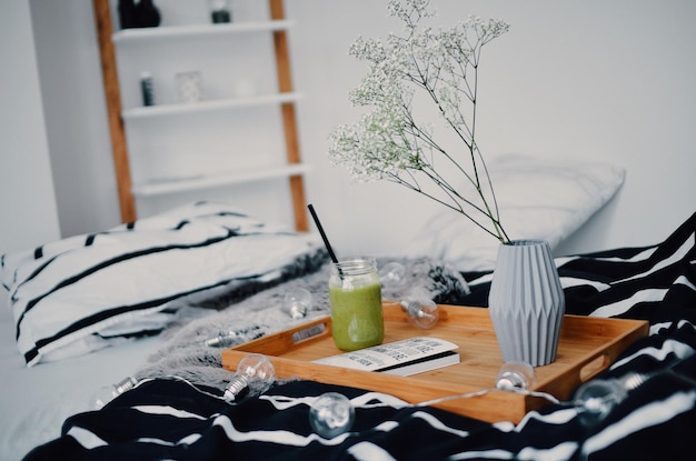 green smoothie by flower vase in tray on decorated bed at home