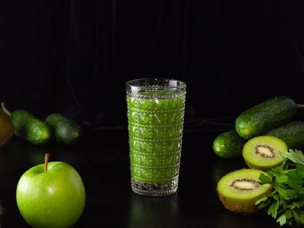 Green smoothie in a glass glass on a black background. Kiwi, apples,cucumbers and greens. Cooking healthy food.