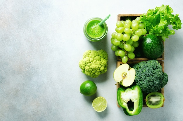 Green smoothie in glass jar with fresh organic green vegetables and fruits on grey. Spring diet, healthy raw vegetarian, vegan concept, detox breakfast, alkaline clean eating. Copy space