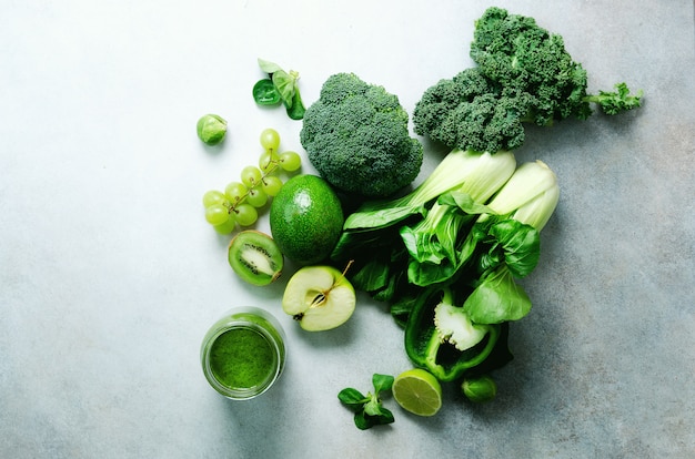 Green smoothie in glass jar with fresh organic green vegetables and fruits on grey 