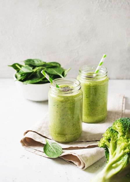 Green smoothie in glass jar with straw and spinach and broccoli