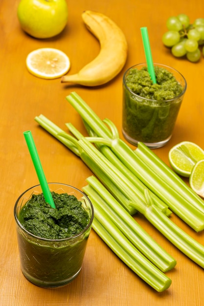 Green smoothie and straw in glasses Celery stalks and banana on table