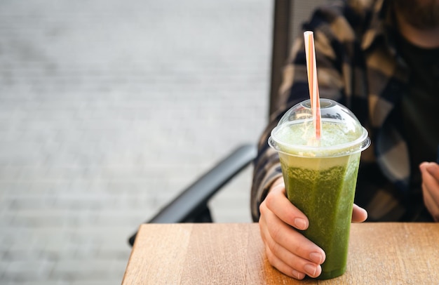 Зеленый смузи на столе в кафе Здоровый мужчина пьет детокс-диету протеиновый коктейль Рука держит пластиковую чашку с овощным соком