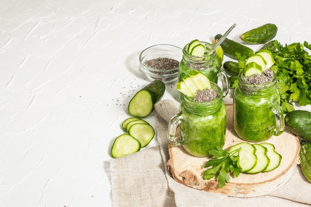 Green smoothie with cucumber in a glass jar. Fresh ripe vegetables, greens, and chia seeds. Trendy hard light, dark shadow. White putty background, copy space