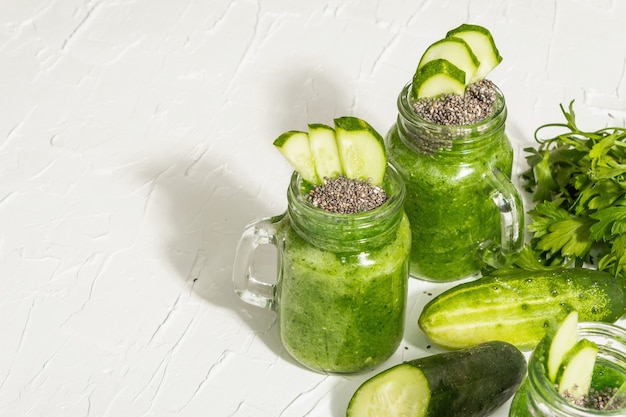Photo green smoothie with cucumber in a glass jar. fresh ripe vegetables, greens, and chia seeds. trendy hard light, dark shadow. white putty background, copy space
