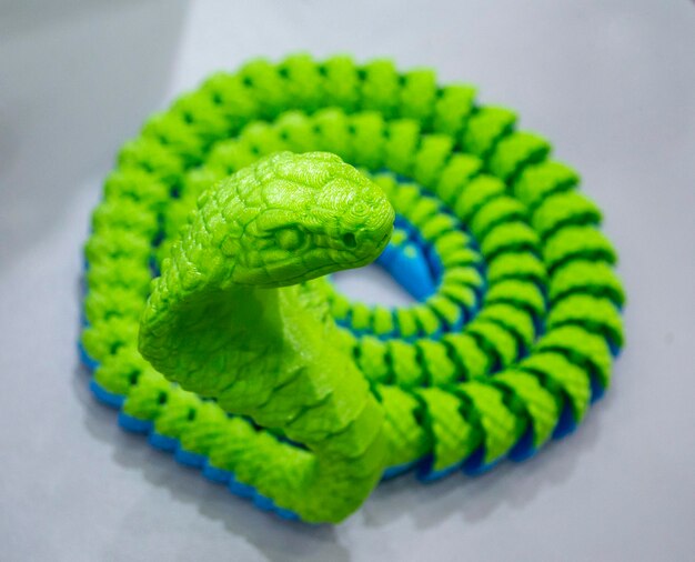 写真 溶けたプラスチックの蛇形の物体からdプリンターで印刷された緑のヘビのおもちゃモデル