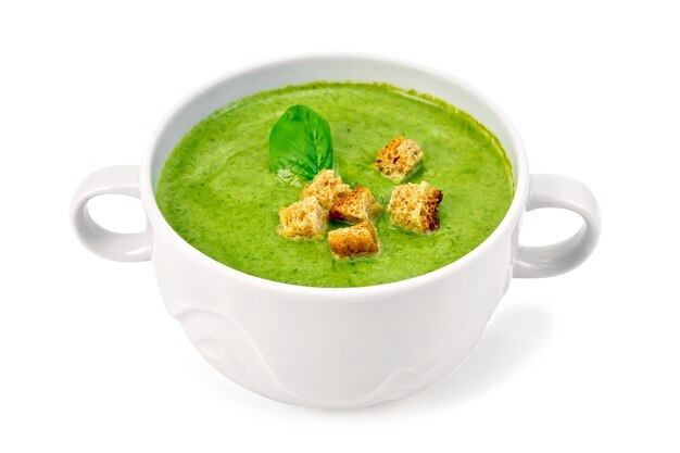 Green soup puree in a white bowl with croutons and spinach leaves isolated